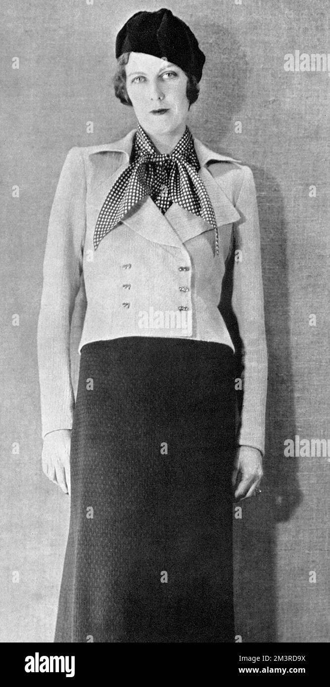 Mrs Richard Norton modelling an 'enchanting ensemble from Schiaparelli, which consists of a short, fitted jacket of tweed in a dull shade of pink and a dress of brown wool with a sleeveless bodice and a flowing tie of dotted crepe de Chine to match.     Date: 1937 Stock Photo