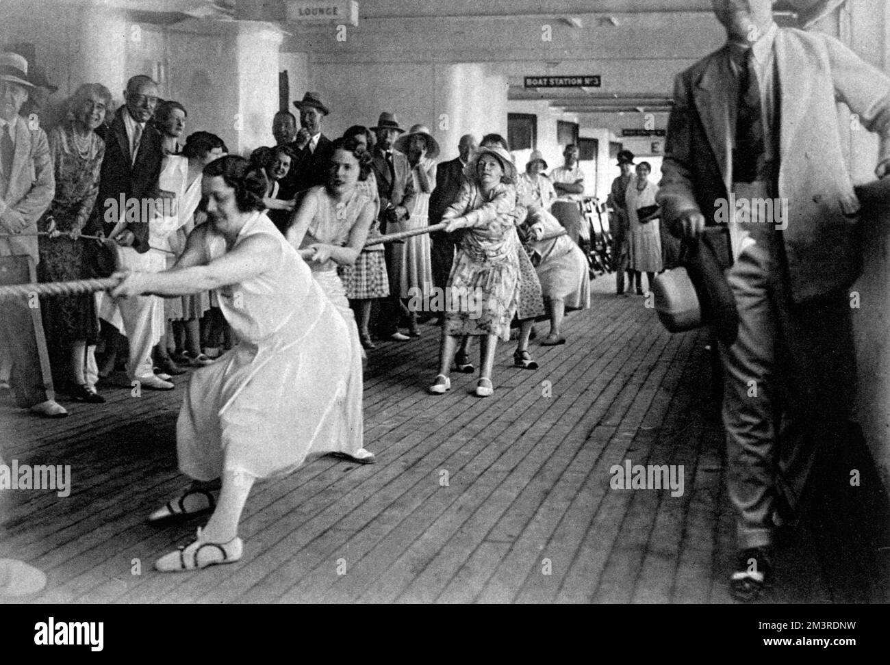 A married versus single tug o' war match on board the R.S.M.P. Atlantis.  The Hon. Mrs Geoffrey Borwick and Lady Moira Combe (nearest the camera) pulling, while the Earl and Countess of Stradbroke (left, hatless) watch proceedings.     Date: 1931 Stock Photo