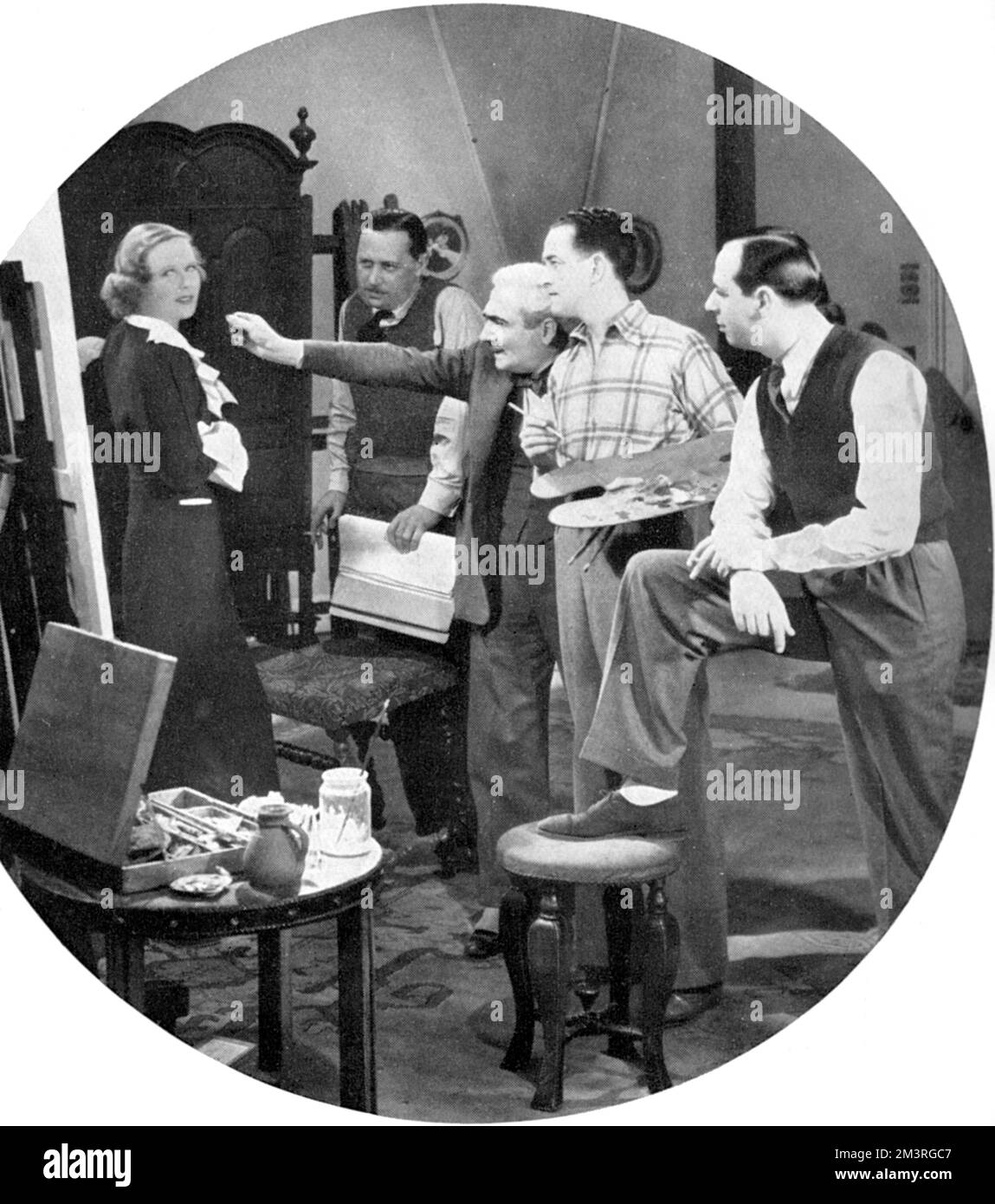 The Italian-born artist, Fortunino Matania, leading illustrator for The Sphere magazine, pictured giving professional hints to actor Gene Gerrard on the set of the new John Stafford film, Susie in the Bath (later remained There Goes Susie) in which he was playing the role of a painter.  Also pictured is the actress Wendy Barrie as a model.       Date: 1934 Stock Photo