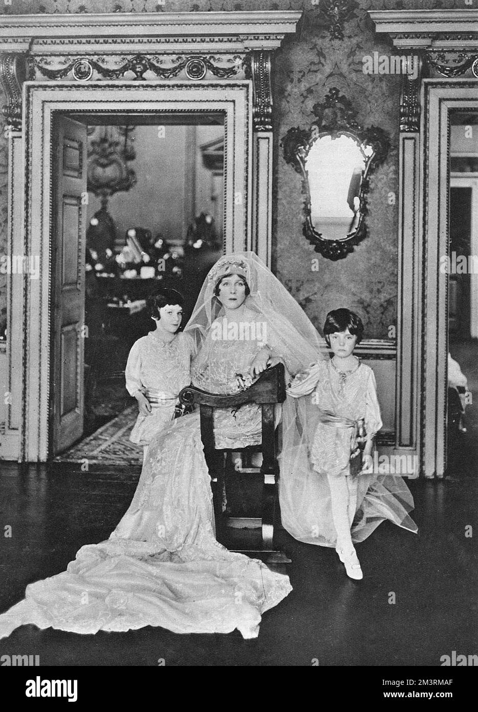 Lady Diana Cooper (nee Manners) posed at her family's London home in Arlington Street in her wedding gown of gold tissue overlaid with lace.  She is attended by her pages, Lord Elcho and the Hon. Michael Charteris, her nephews, the sons of her sister the former Lady Violet Manners.       Date: 1919 Stock Photo