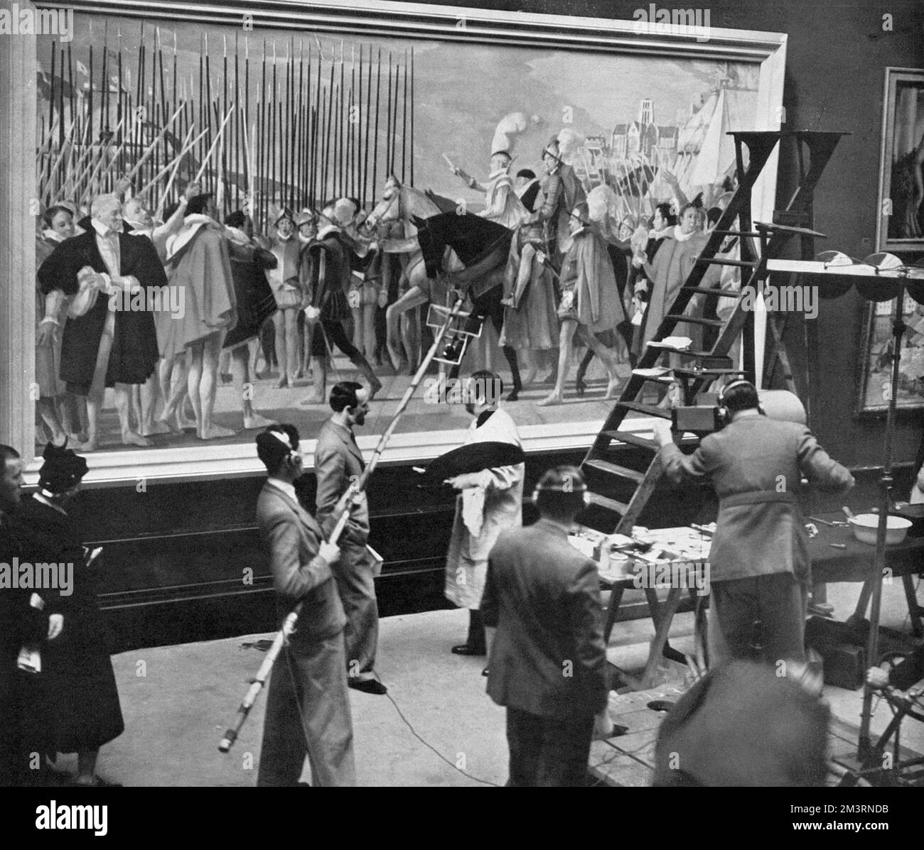 Televising varnishing day at Burlington House: viewers watch artists put the finishing touches to their pictures in readiness for the Royal Academy opening, 1939. A TV camera focuses on A.K. Lawrence in front of his painting of Queen Elizabeth with her Armies. Stock Photo