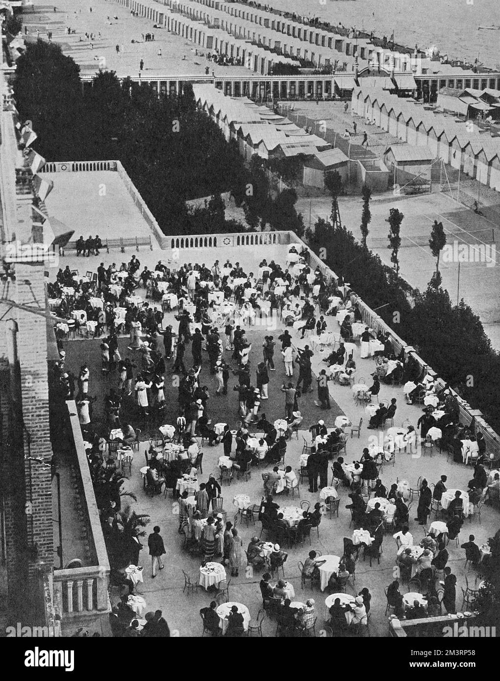An aerial view over the Hotel Excelsior at the fashionable Venetian Lido, frequented by high society.  Photograph shows a th&#x9824;ansant in progress and waiters serving people at a number of tables.  Beyond that the beach with changing tents and beach huts in evidence.     Date: 1925 Stock Photo