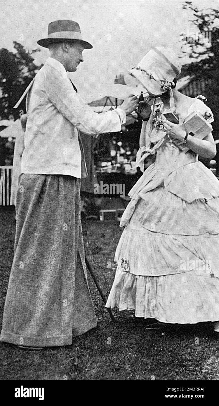 The logical development of the Oxford bags demonstrated at Regent's Park in 1925. The gentleman shown was one of the participants in the Old English Garden Fete in the Royal Botanic Gardens in Regent's Park. His trousers were stated to have measured 48 inches around the bottom. He's seen here giving a light to a lady in Victorian dress.     Date: 1925 Stock Photo