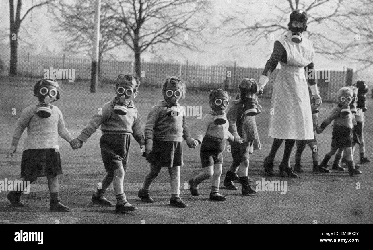 London babies find peace in the country: a nurse walks evacuated children in gas masks across a playground, to accustom them to the wearing of gas masks. LCC Residential School near Windsor.     Date: 1941 Stock Photo