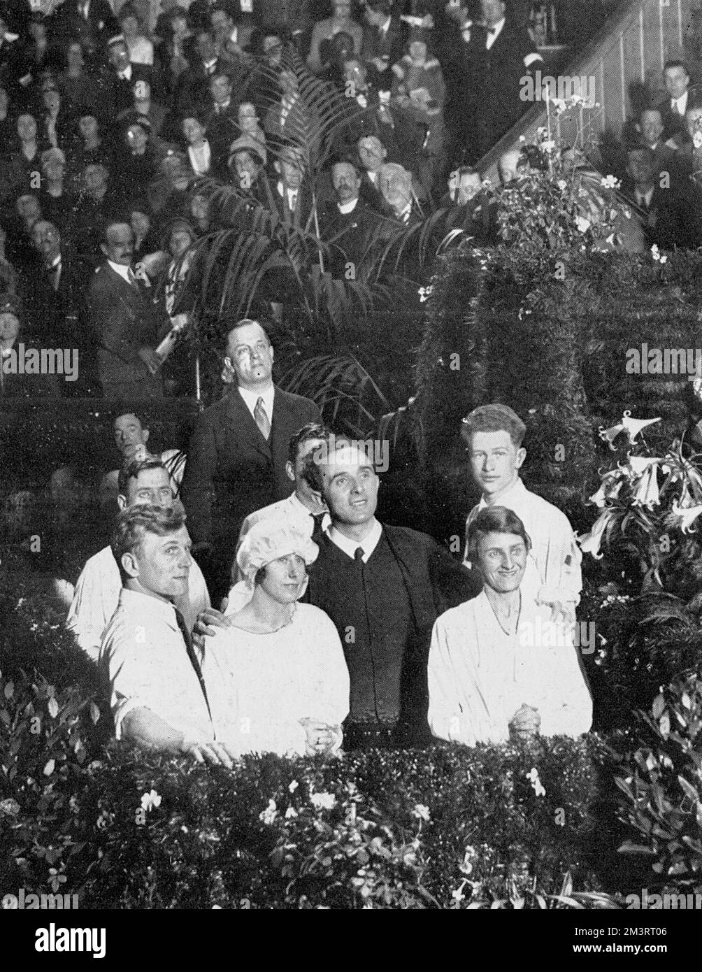 A public baptismal ceremony at the Albert Hall on Good Friday, 1928, where nine hundred men and women of the Elim Foursquare Gospel Alliance were immersed in a tank of warm water.  Principal George Jeffreys, the Welsh founder of the sect, is shown here in the flower decked tank with his arms around two of the women converts. Stock Photo
