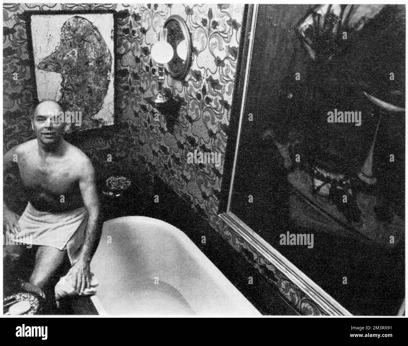 Interior decorator and designer Anthony Denney pictured in his stunning bathroom.  The walls are covered in an art nouveau still patterned cotton, padded behind, and are hung with pictures by Bernard Dubuffet and Edward Burne-Jones.  A porcelain kangaroo offers soap to the bather.     Date: 1966 Stock Photo