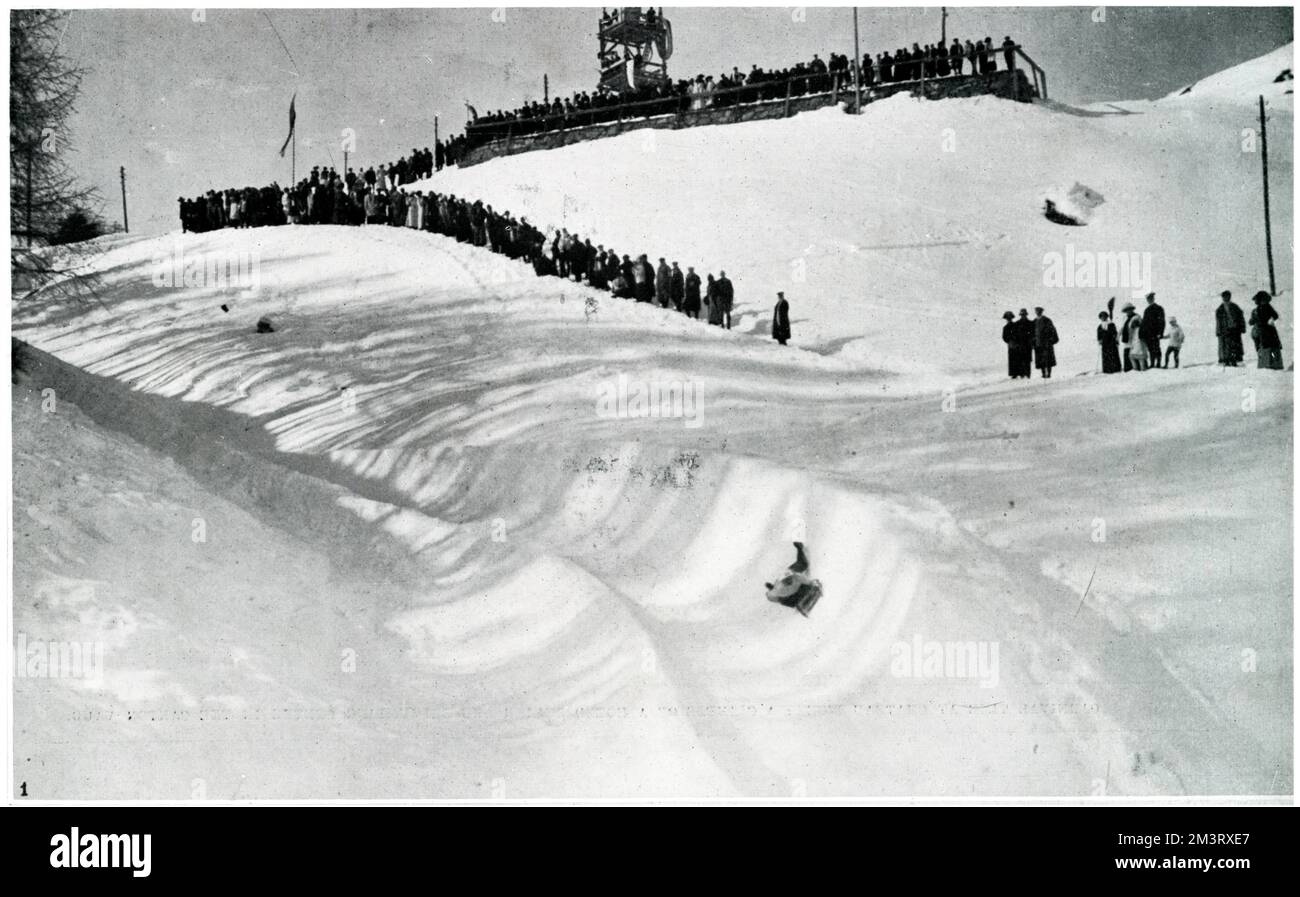 Daredevil tobogganists take a thrilling turn at the second bank of the Church leap at the famous Cresta Run at St. Moritz with the grand stand visible in the background.      Date: 1924 Stock Photo