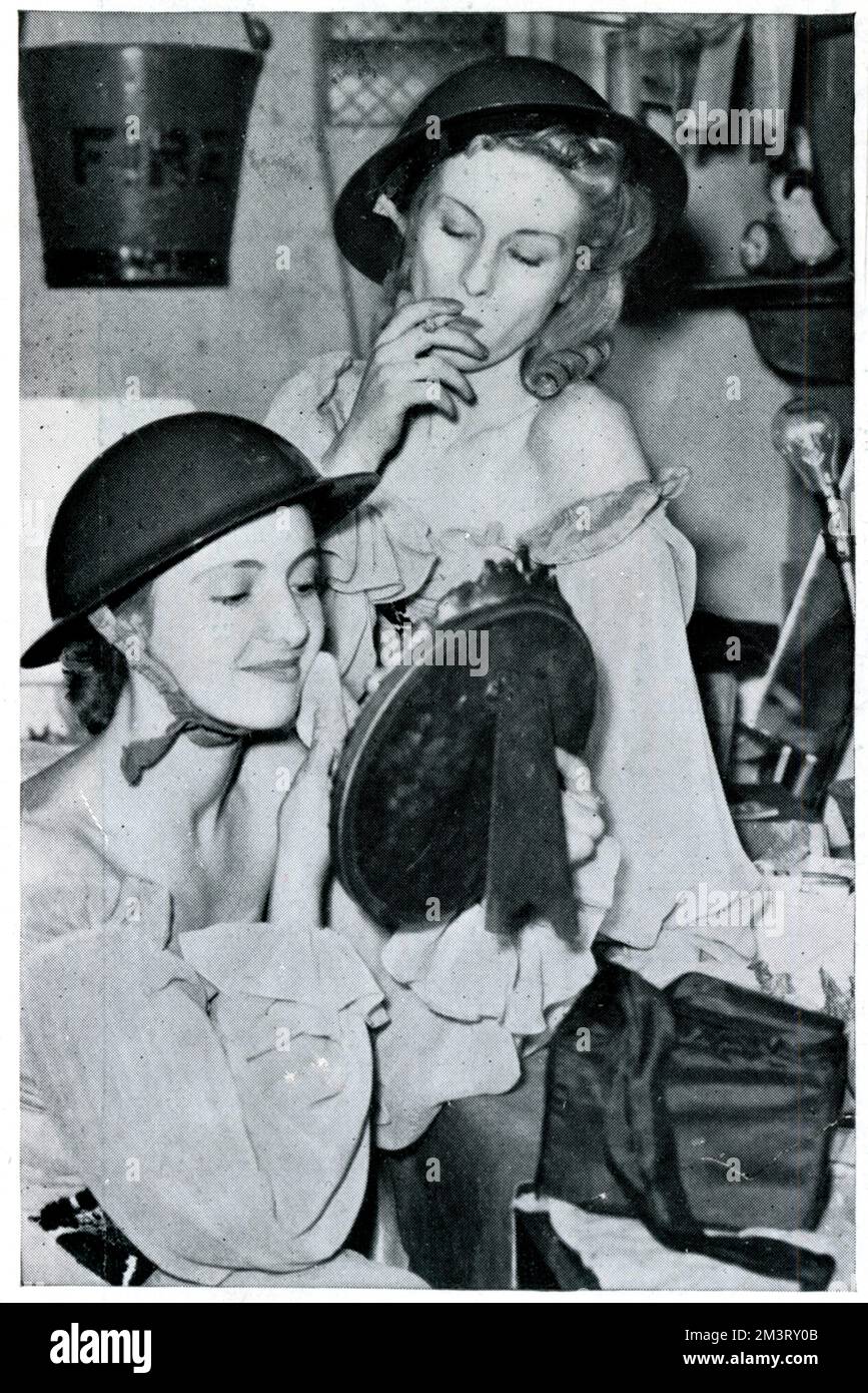 Two women in tin helmets photographed as they prepare for a show at the Windmill Theatre. The Windmill Theatre, which today uses the motto &quot;we never closed&quot;, had just reopened after its only compulsory state-enforced closure between 4th-16th September 1939. The Sphere comments on the &quot;topical&quot; nature of the performance the women were preparing for which featured tin hats and gas masks.     Date: September 1939 Stock Photo