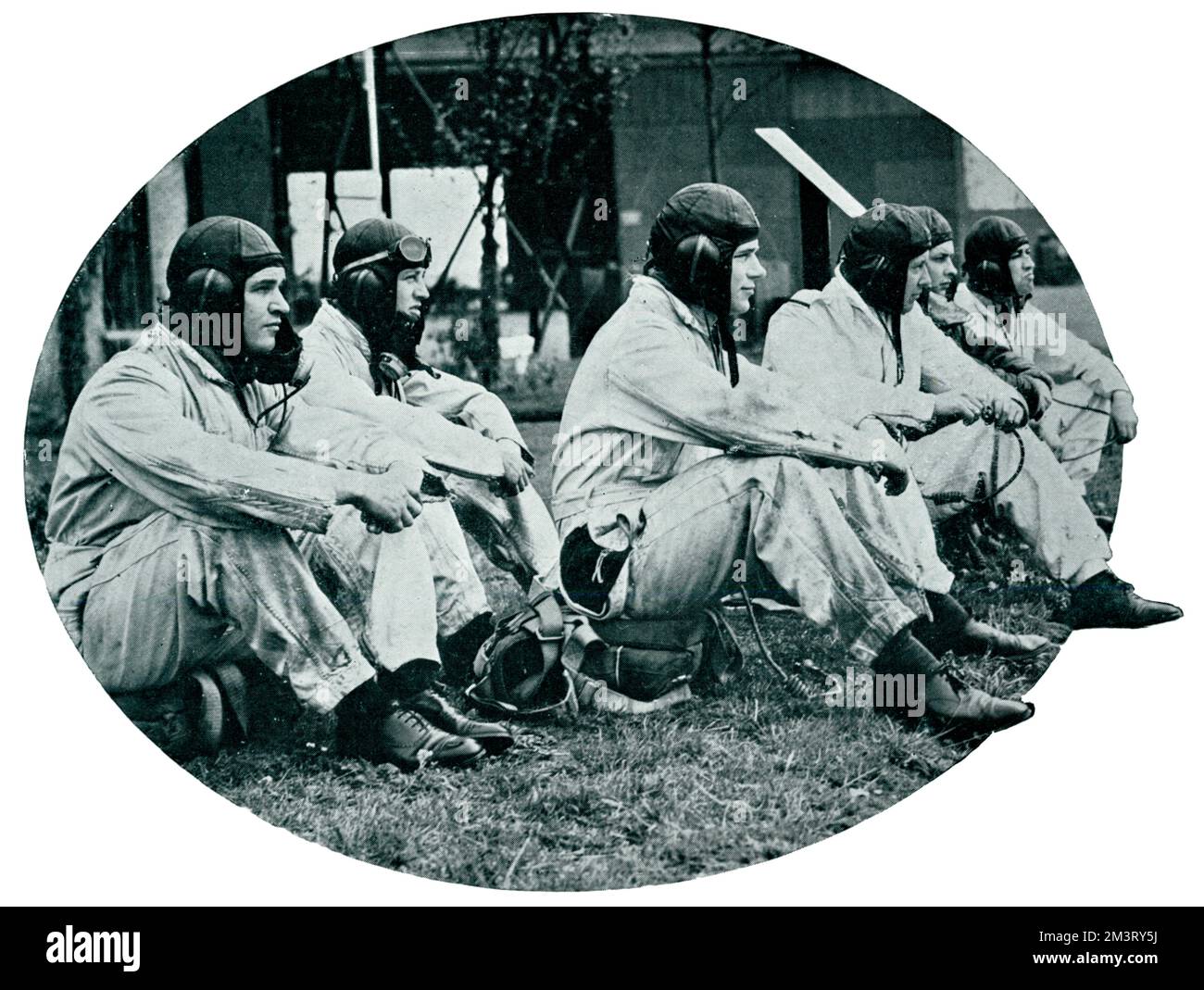 Interceptor aircraft pilots sitting on their parachutes as they wait for the order to fly, a few weeks after the outbreak of war. Interceptor pilots were used to attack enemy planes as they approached and these men are shown in full uniform, complete with earphones and goggles.     Date: 1939 Stock Photo