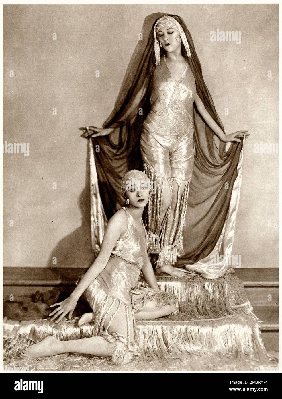 The Dolly Sisters as they perform their Persian dance in the &quot;League of Notions&quot;, a popular revue at the New Oxford. Both wore dancing &quot;silver Persian dresses&quot; with skull-caps and began their performance in a silver chiffon cloak which one of the sisters is still wearing in the picture.  Despite being attractions at the New Oxford, the Dolly Sisters travelled at the end of each show to the London Pavilion in order to perform their Pony Trot in the last scene of &quot;the Fun of the Fayre&quot;.      Date: 1921 Stock Photo