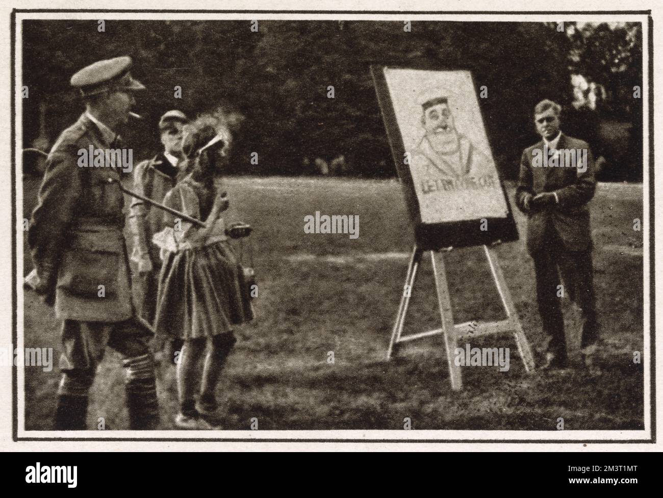The artist John Hassall pictured sketching at a Red Cross fundraising event in Kidbrooke Park, London in 1918. To the left is Major Devitt who organised the sports for men of the Royal Field Artillery. Hassall carried out a huge amount of work for free during the Great War, and regularly made appearances at hospitals and fundraisers where he would make humorous sketches which were often auctioned.     Date: 1918 Stock Photo