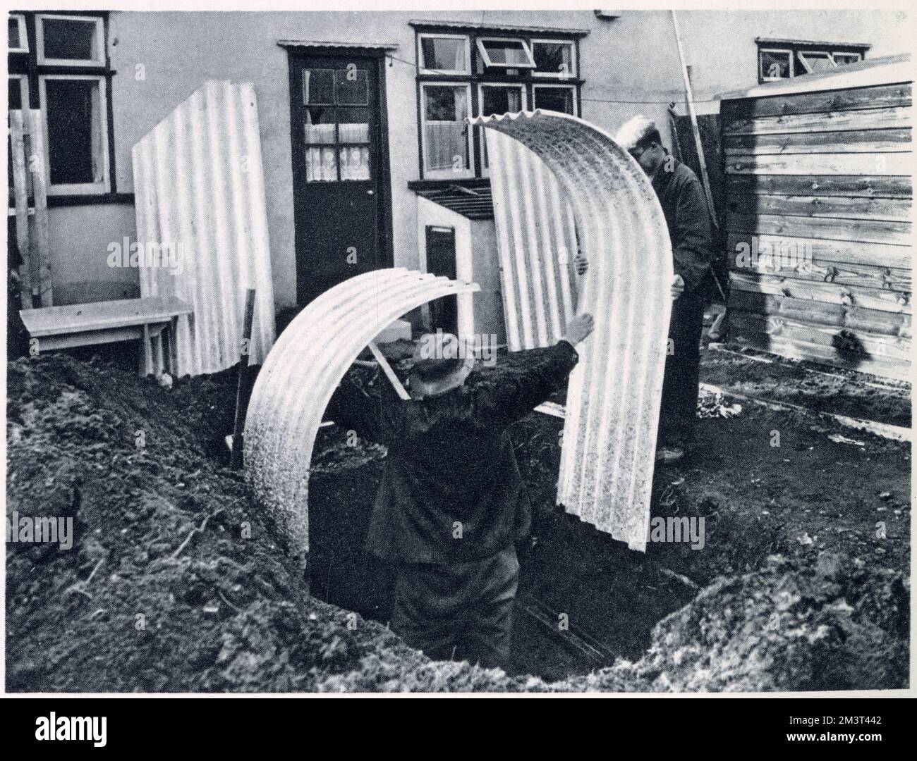 Workmen placing the sections of the Government's steel air-raid shelters in a small garden in Tiber Street, Islington, London. Buried three feet in the ground, standing on steel foundation channels and sections are joined together with nuts and bolts. Stock Photo