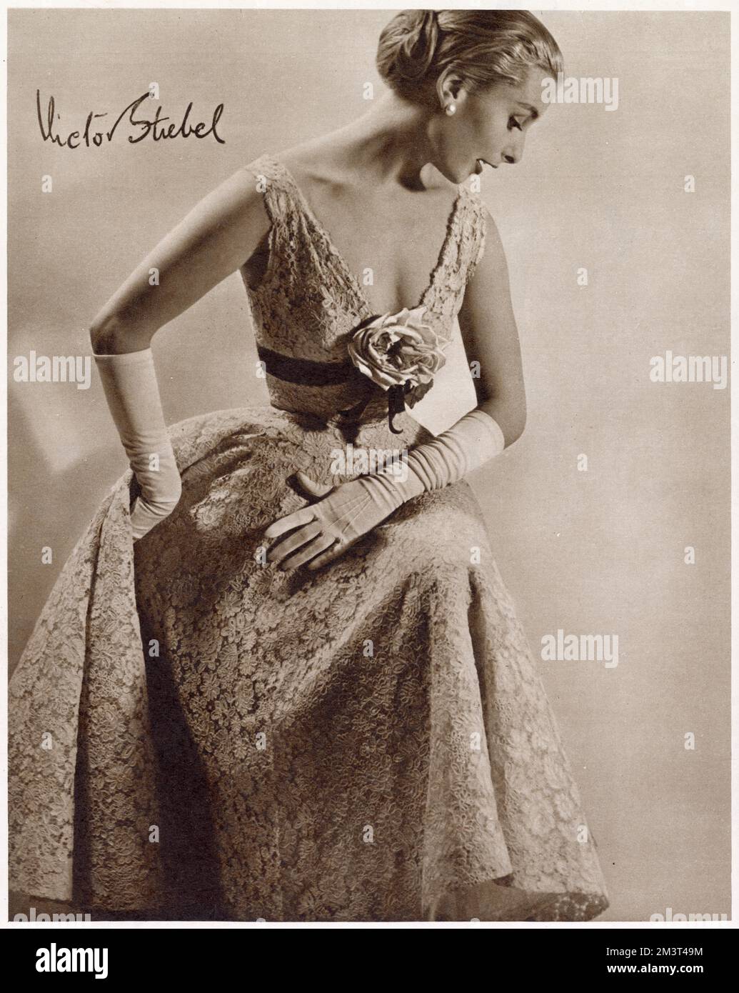 A short, party dress in Birkin's needle-run lace designed by Victor Stiebel at Jacqmar The empire line waist band is tied with a ribbon and a drooping rose. Stock Photo