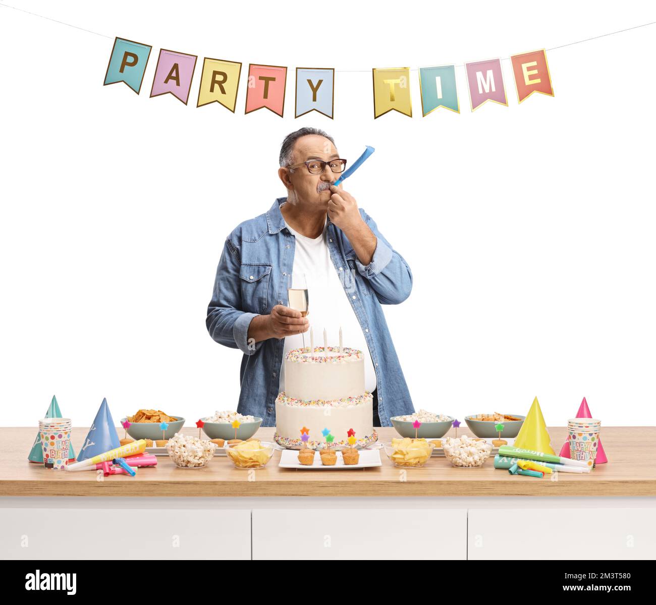 Casual mature man blowing a party horn behind a counter with cake isolated on white background Stock Photo