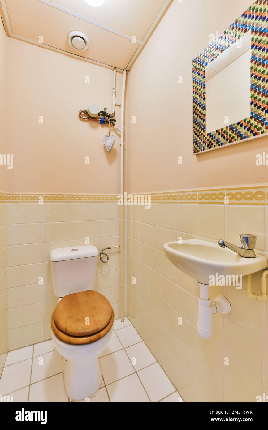 a bathroom with a toilet, sink and mirror on the wall next to it is a wooden seat that has been removed Stock Photo