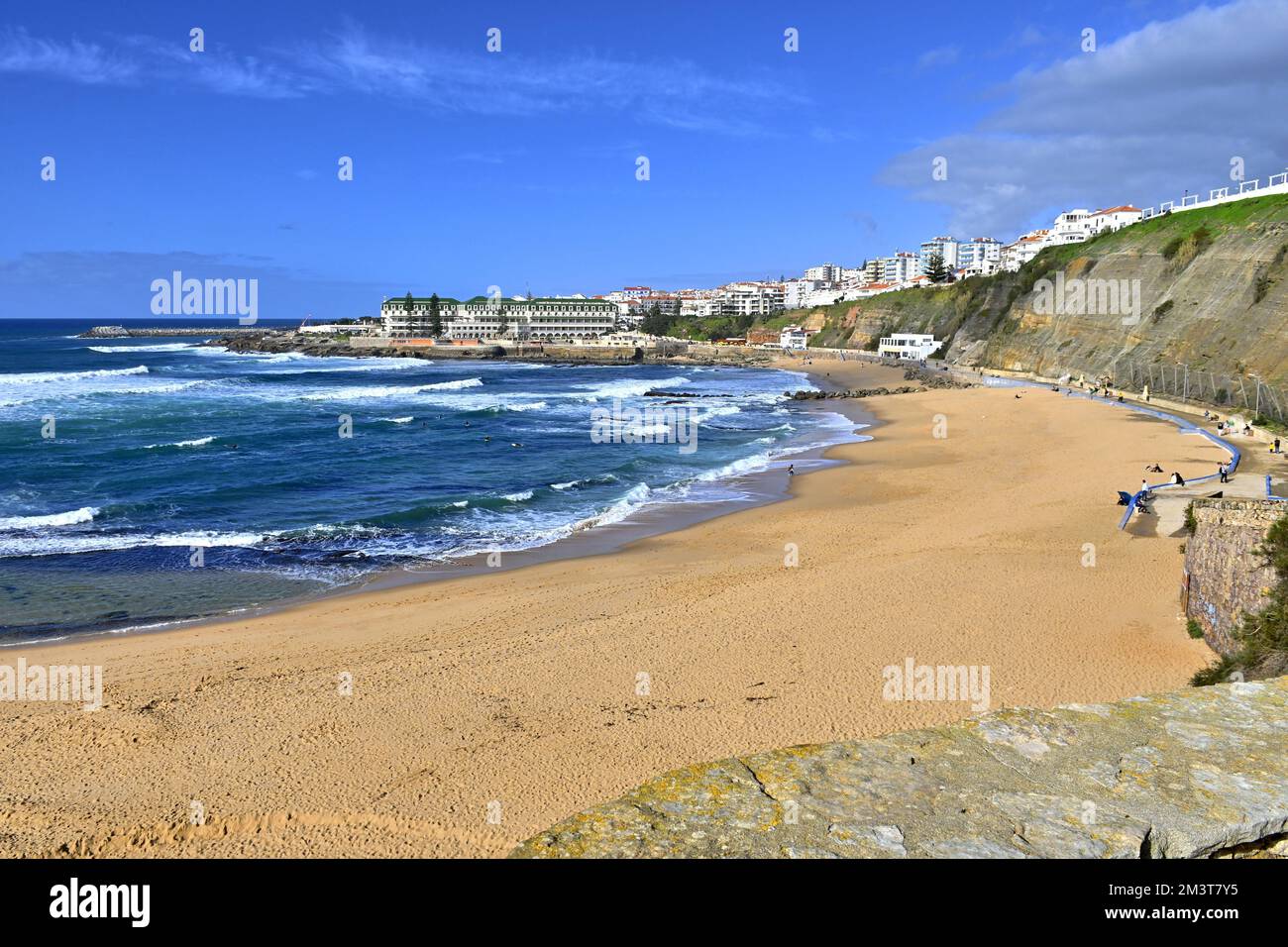 A scenic landscape of sandy Baleia beach and buildings in distance in Ericeira, Portugal on sunny day under blue sky Stock Photo