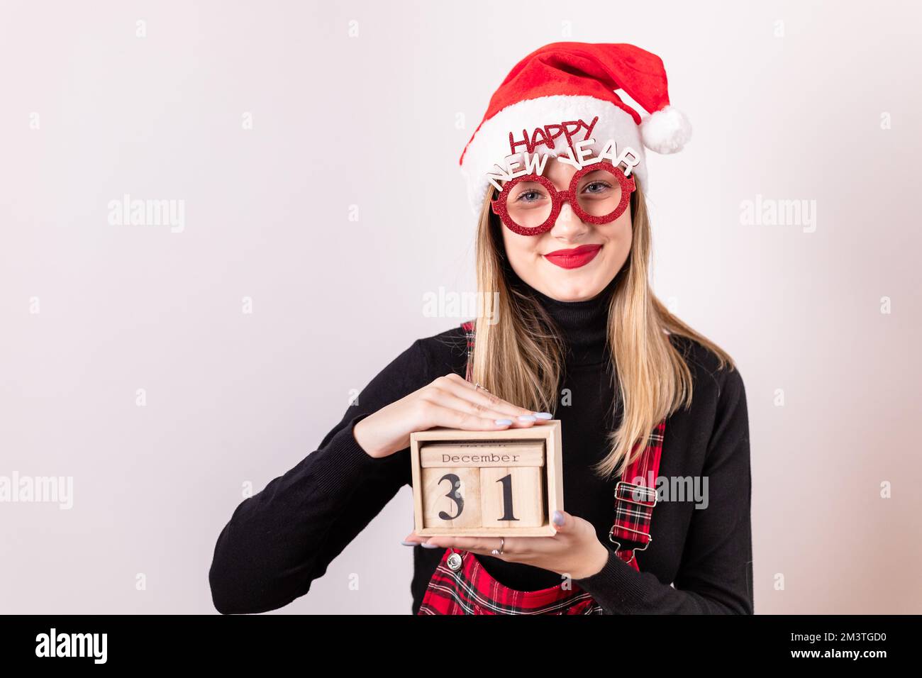Beautiful, young, blonde girl with Santa hat and prop glasses holding a wooden calendar date box. December 31st Stock Photo