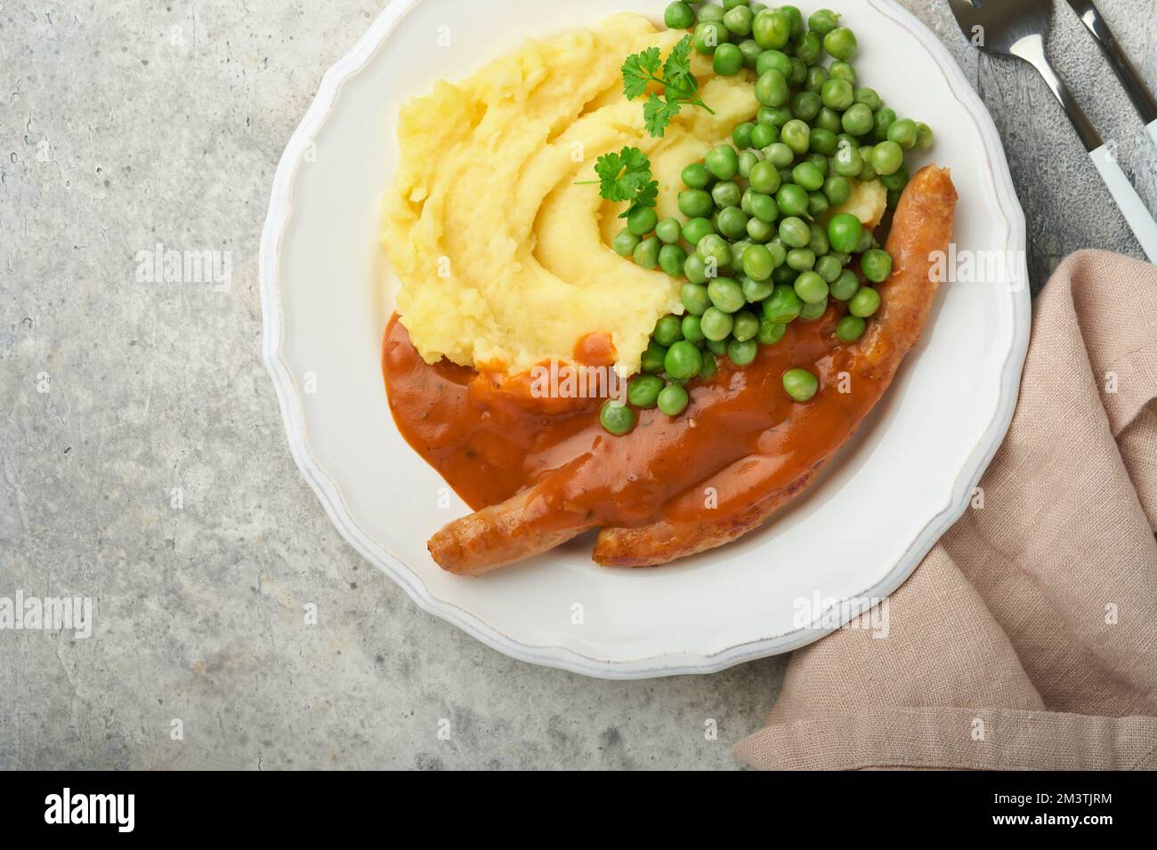 Bangers and mash. Grilled sausages with mash potato and green pea on white plate on grey background. Traditional dish of Great Britain and Ireland. BB Stock Photo