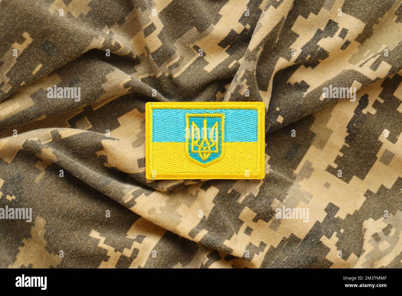 Pixeled digital military camouflage fabric with ukrainian flag and coat of arms on chevron in blue and yellow colors. Attributes of ukrainian soldier uniform Stock Photo