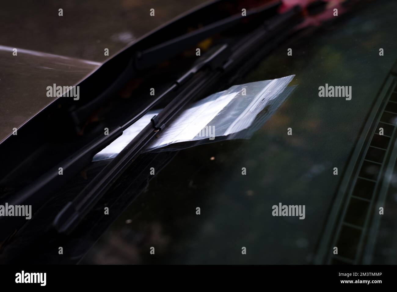 Parking ticket in plastic ziplock bag under car wiper on windshield