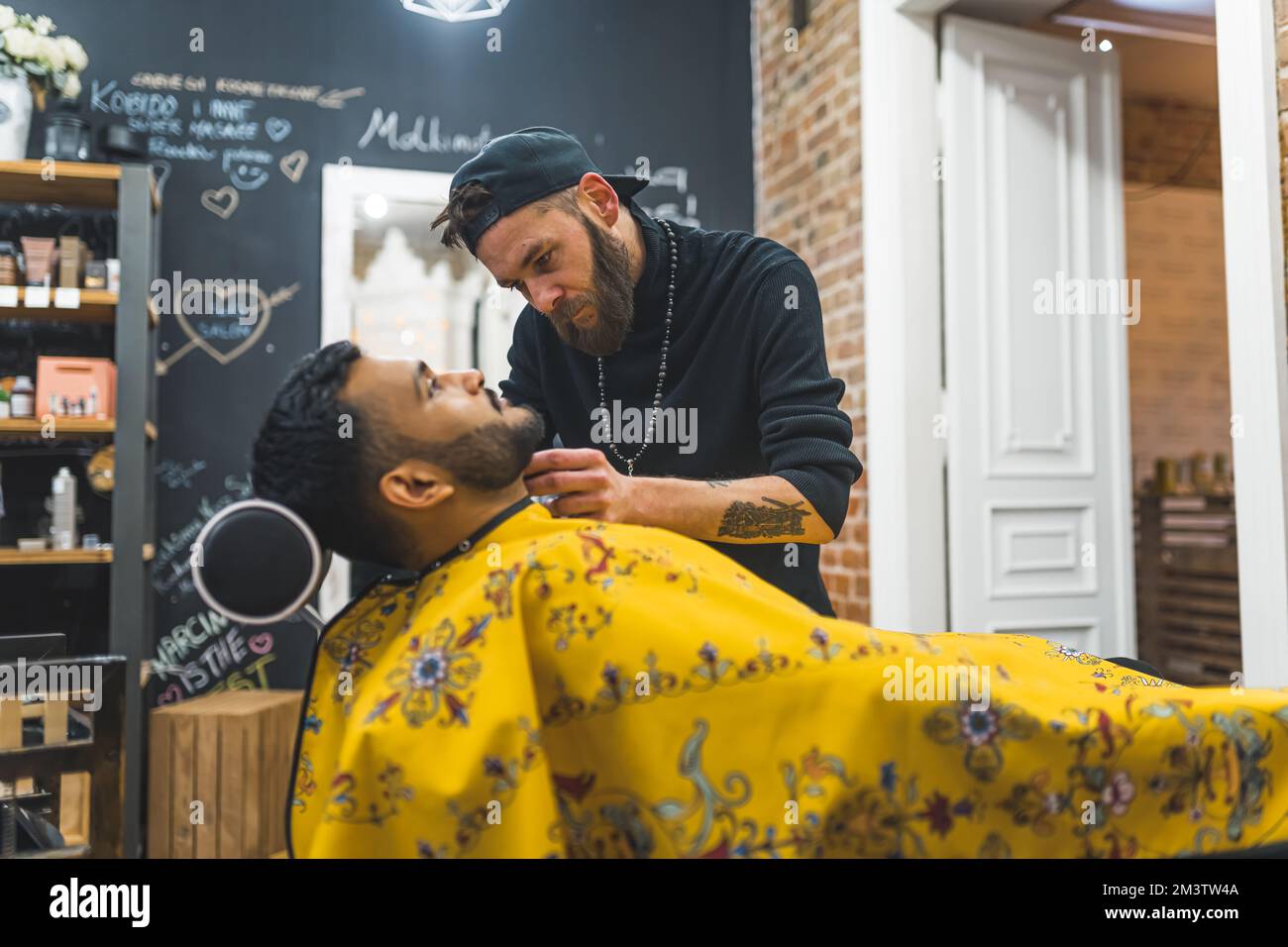 Side view of a barber trimming his client beard with an electric shaver