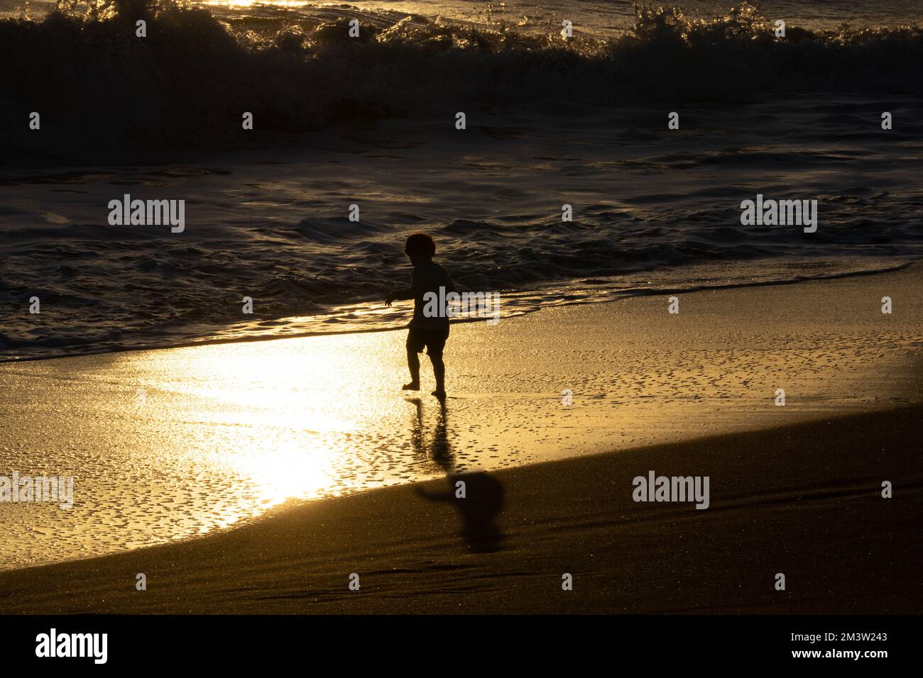 Wanganui New Zealand - April 9 2022; Walking legs of Unrecognizable Young person at waters edge on surf beach in silhouette back-lit by sunset Stock Photo