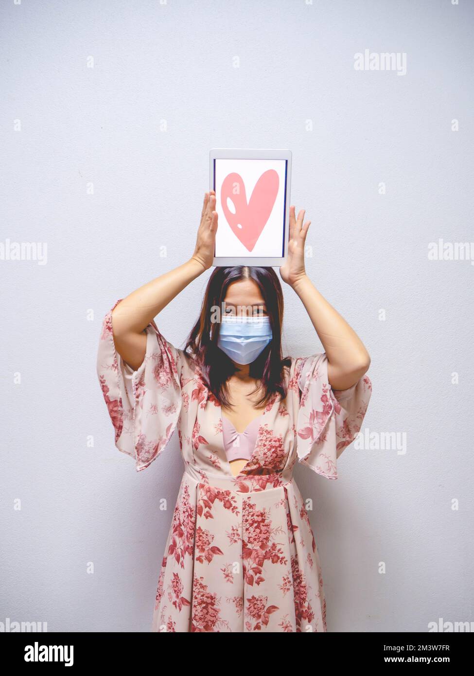 A woman wearing a mask and holding a heart shaped tablet. Stock Photo