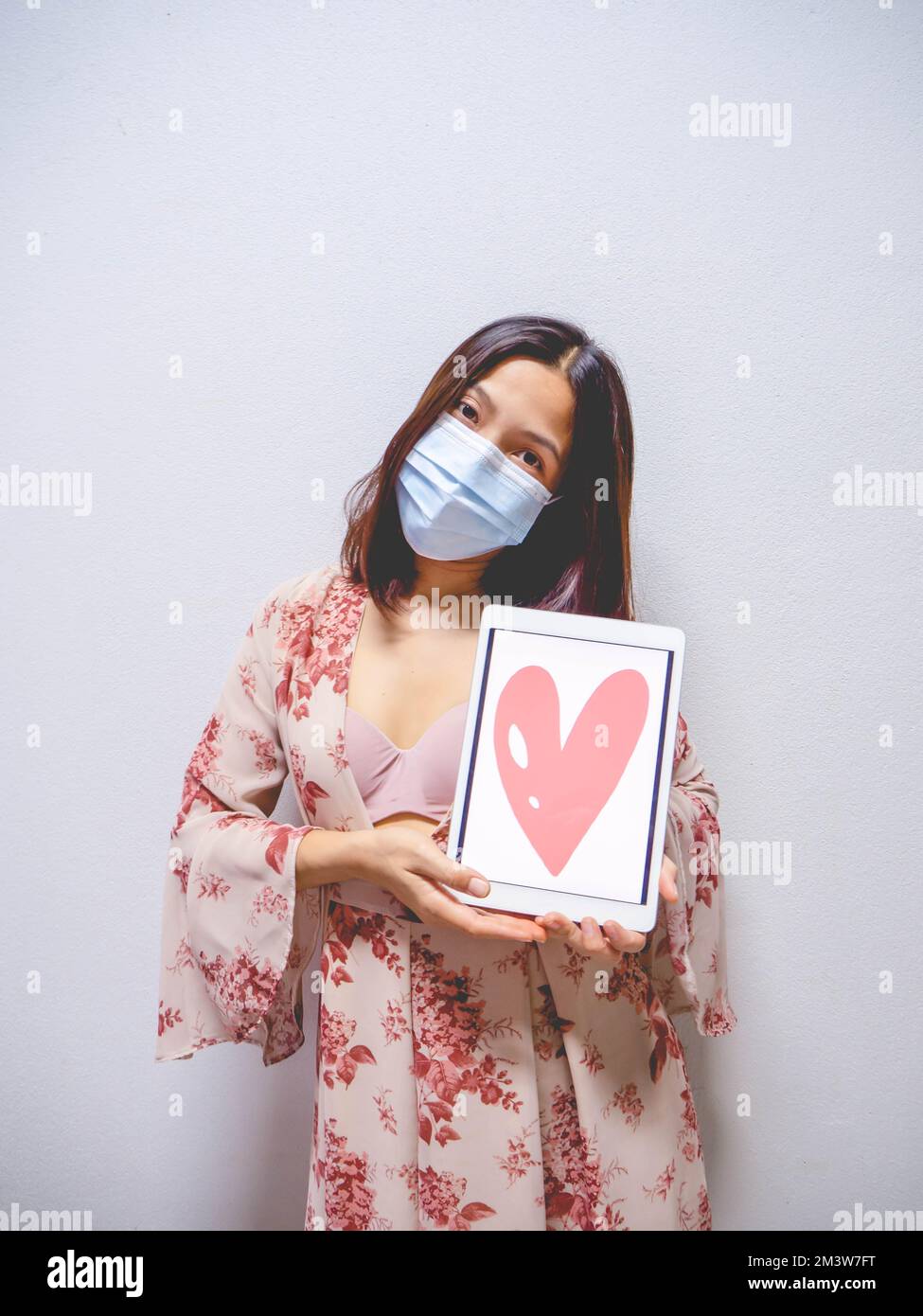 A woman wearing a mask and holding a heart shaped tablet. Stock Photo