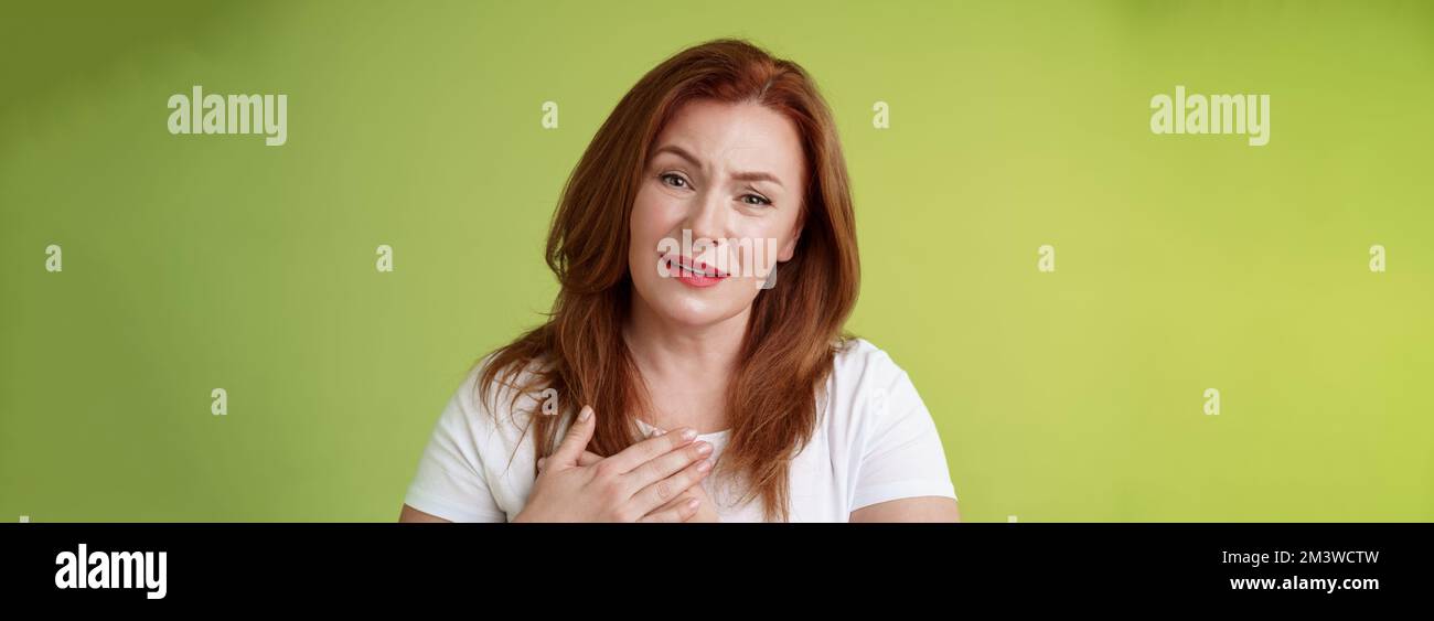 Story touched lady heart. Tender impressed middle-aged redhead woman press palms chest sighing happily look heartwarming temptation smiling appreciate Stock Photo