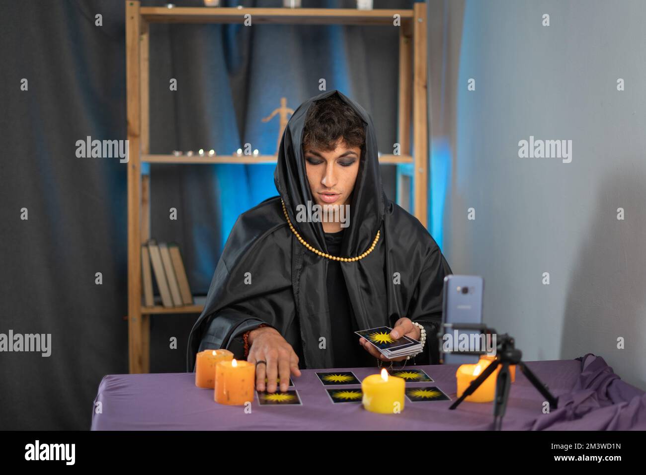 Male fortune teller reads tarot cards for predictions, telling customers using web cam by providing services online via mobile phones, new service Stock Photo
