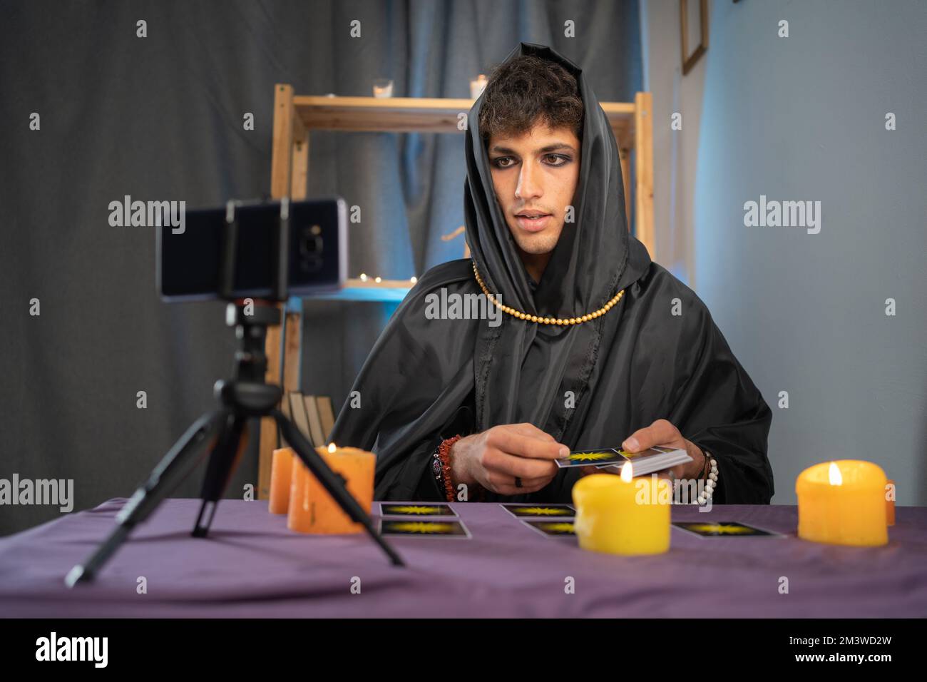 New service concept. Male fortune teller in magician costume reads tarot cards for predictions, telling customers using web cam by providing services Stock Photo