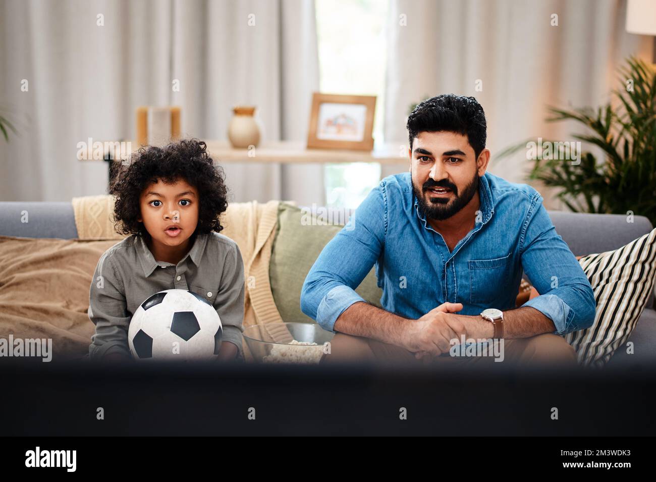 The match is starting liven up now. an adorable little boy watching a football game with his father on tv at home. Stock Photo