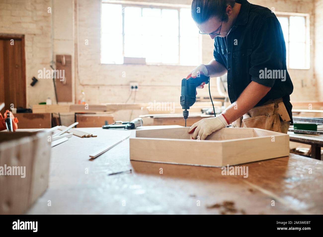 Just making some final adjustments to the masterpiece. a handsome young carpenter using an electric drill while working inside a workshop. Stock Photo
