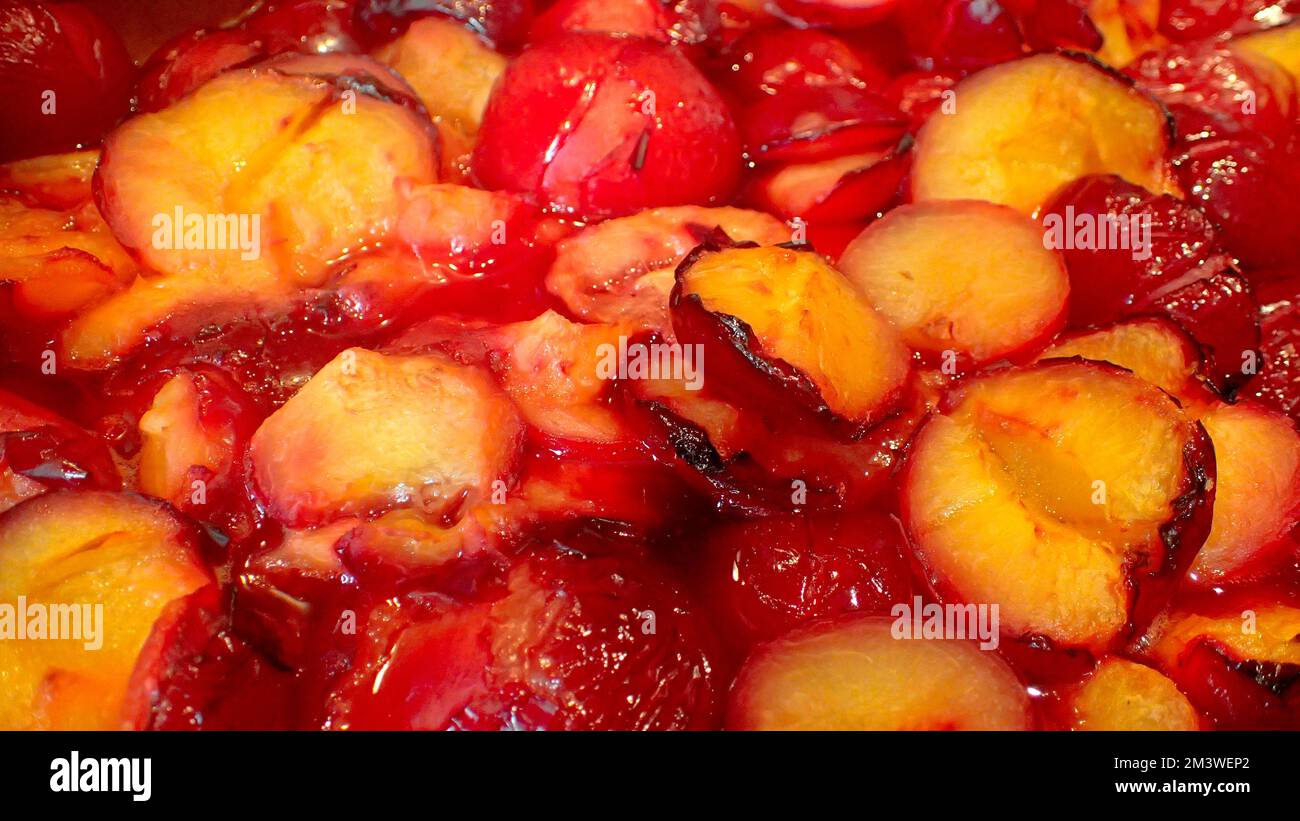 Halved and roasted yellow fleshed red plums gently boiling in a large pot.  The reduction will make plum sauce. Stock Photo