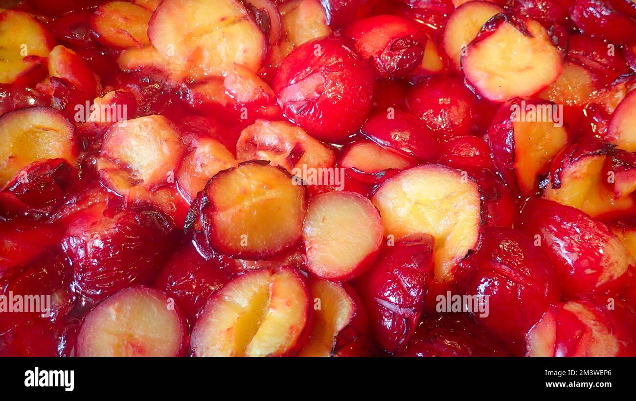 Halved and roasted yellow fleshed red plums gently boiling in a large pot.  The reduction will make plum sauce. Stock Photo