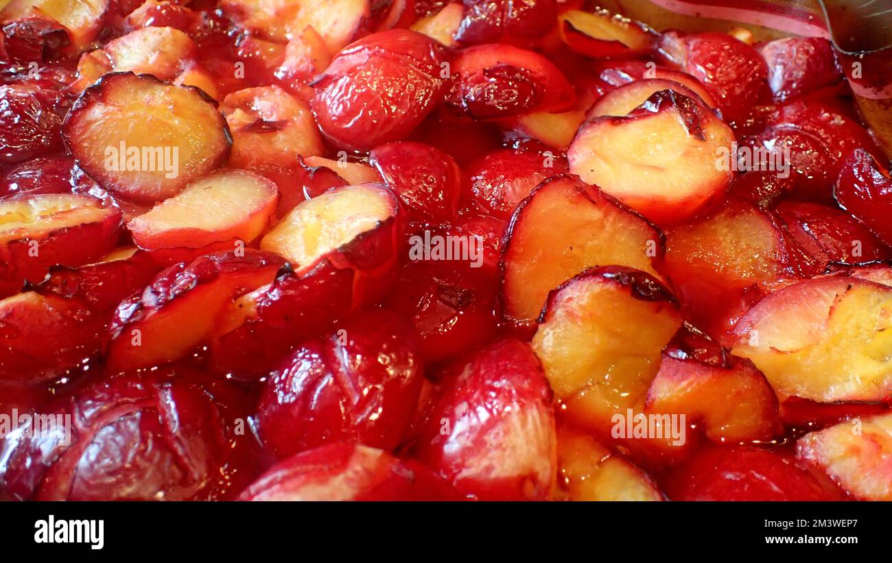 Halved and roasted yellow fleshed red plums gently boiling in a large pot.  The reduction will make plum sauce. Stock Photo