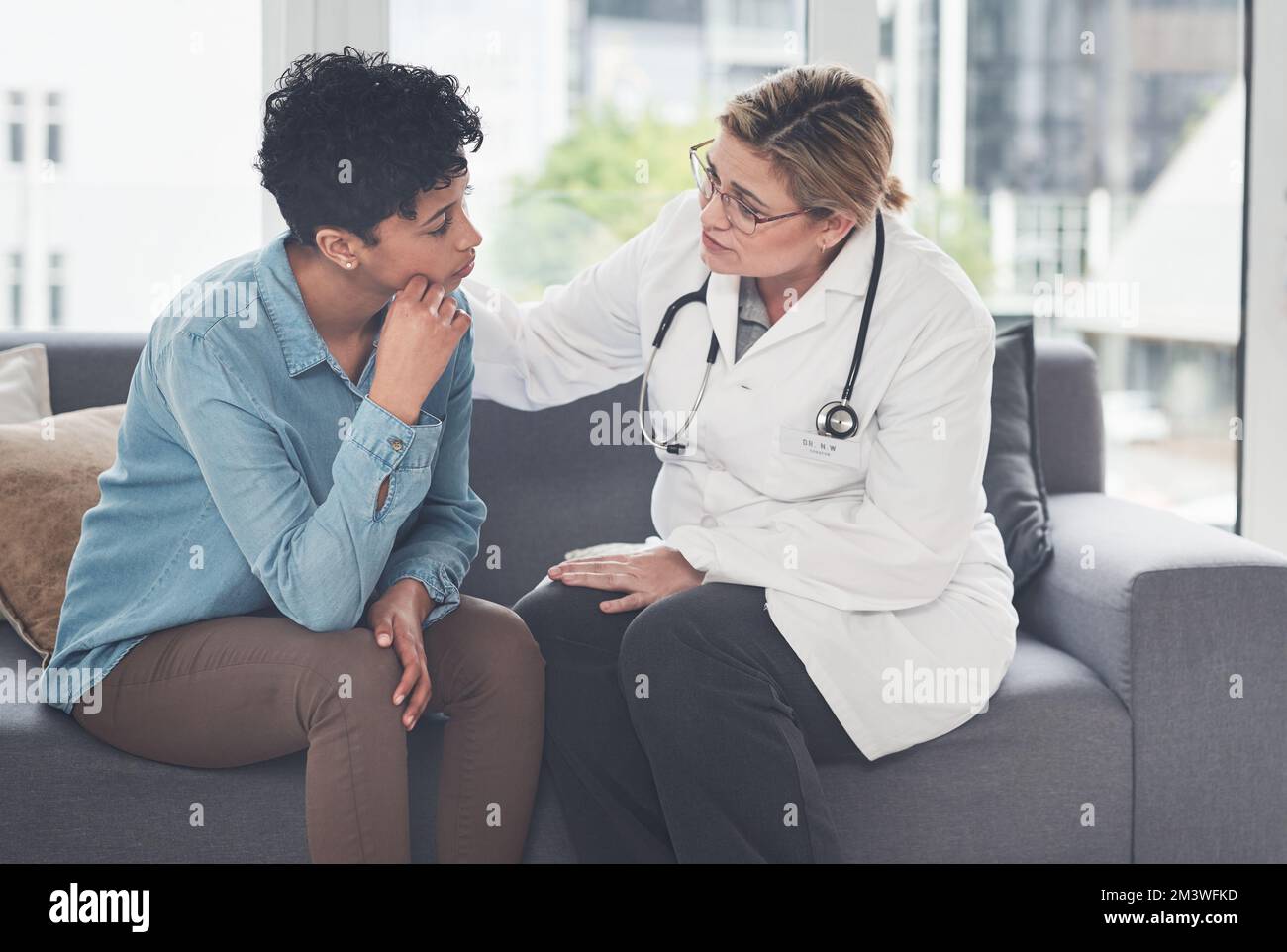 You will overcome this...a compassionate young female doctor consoling a female patient while sitting on the couch in her office. Stock Photo
