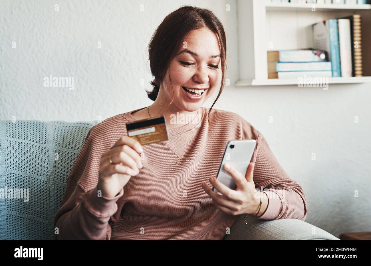 I budgeted for this item. an attractive young woman sitting on her home sofa alone and using her cellphone for online shopping. Stock Photo