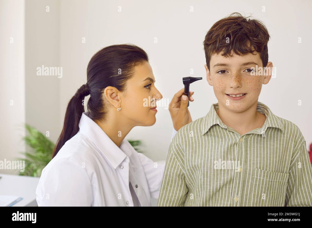 Otorhinolaryngologist uses otoscope to examine child's ear during medical examination in hospital. Stock Photo