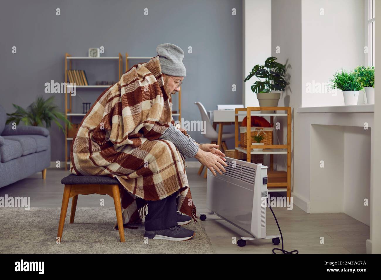 Elderly man wrapped in plaid feeling cold at home Stock Photo