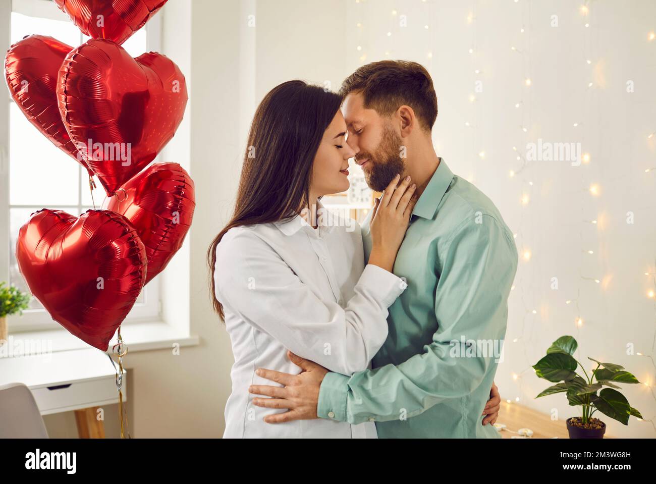 Happy couple kissing while standing in room with red heart shaped ...