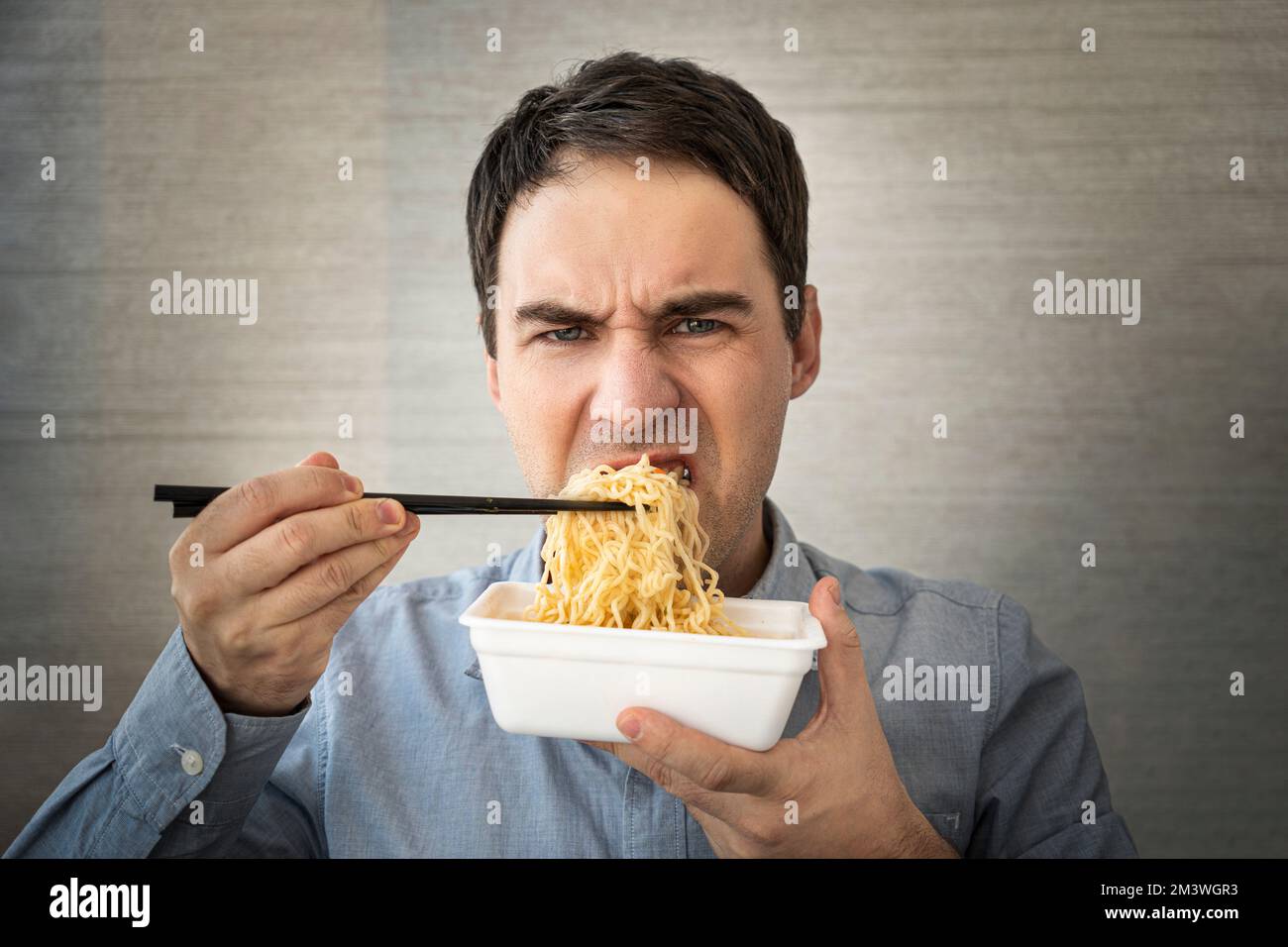 Young man eating instant noodles while working with in office. Lunch at the office. tasteless junk food Stock Photo