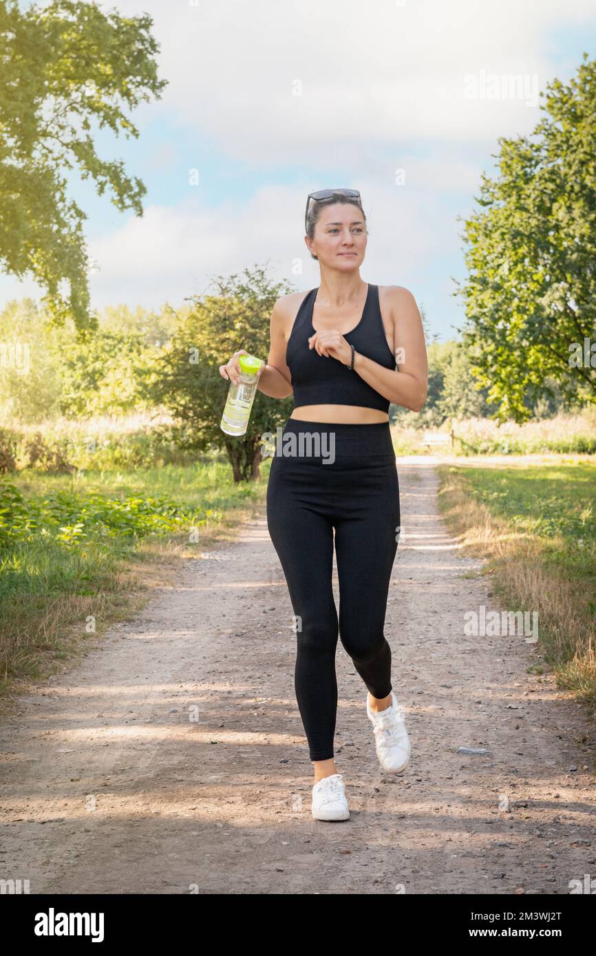 Young beautiful woman in black uniform jogging in summer park. Horizontal portrait. Stock Photo