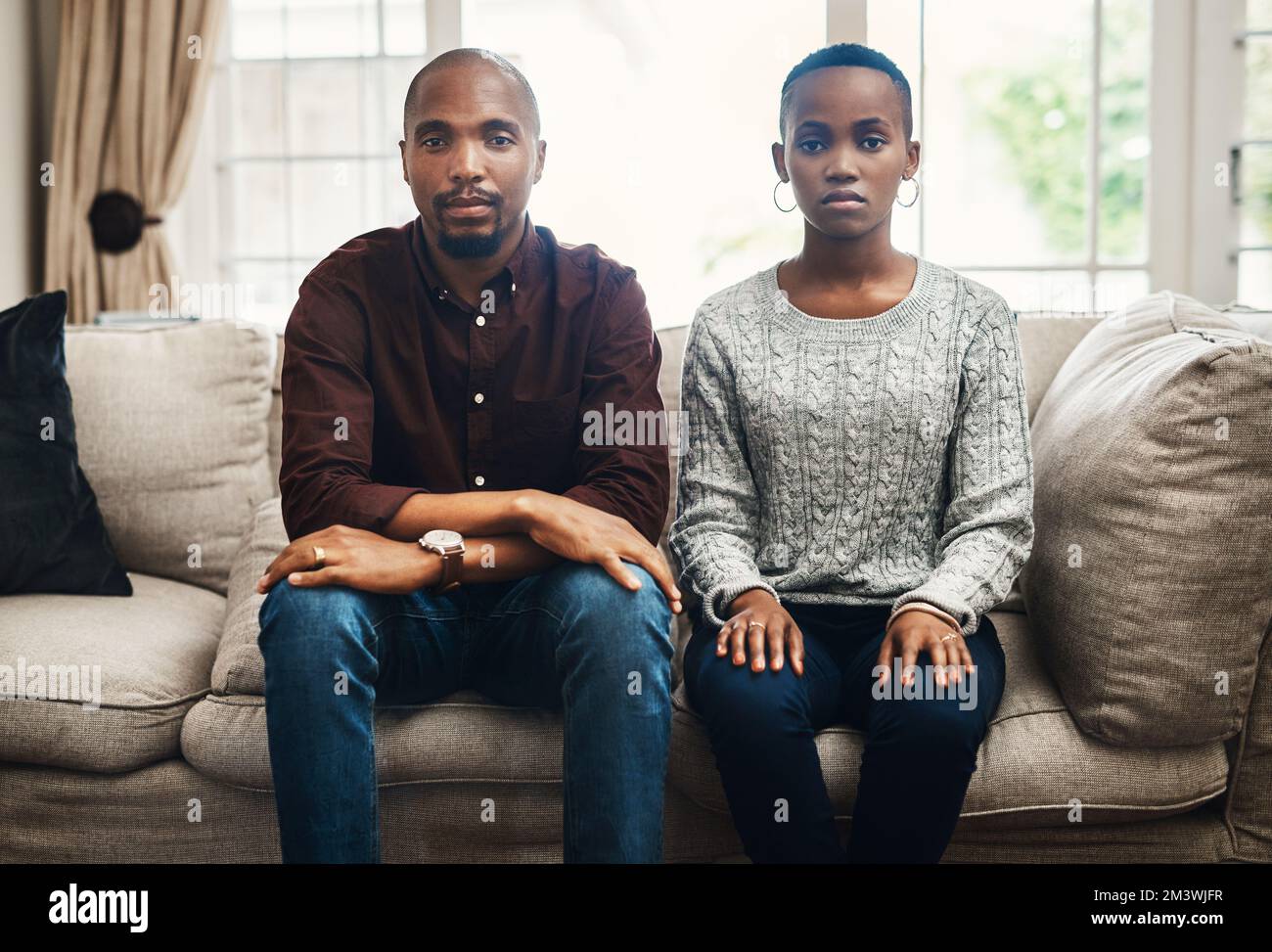 Were bold and unapologetic about our love. Portrait of a young couple looking serious and sitting alongside each other on a sofa at home. Stock Photo