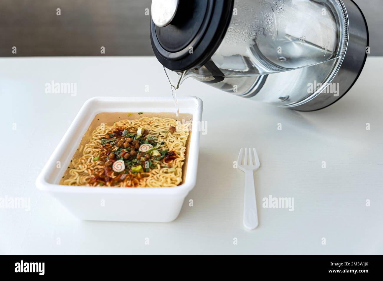 Boiling water from the kettle is filled with instant noodles in a box ...