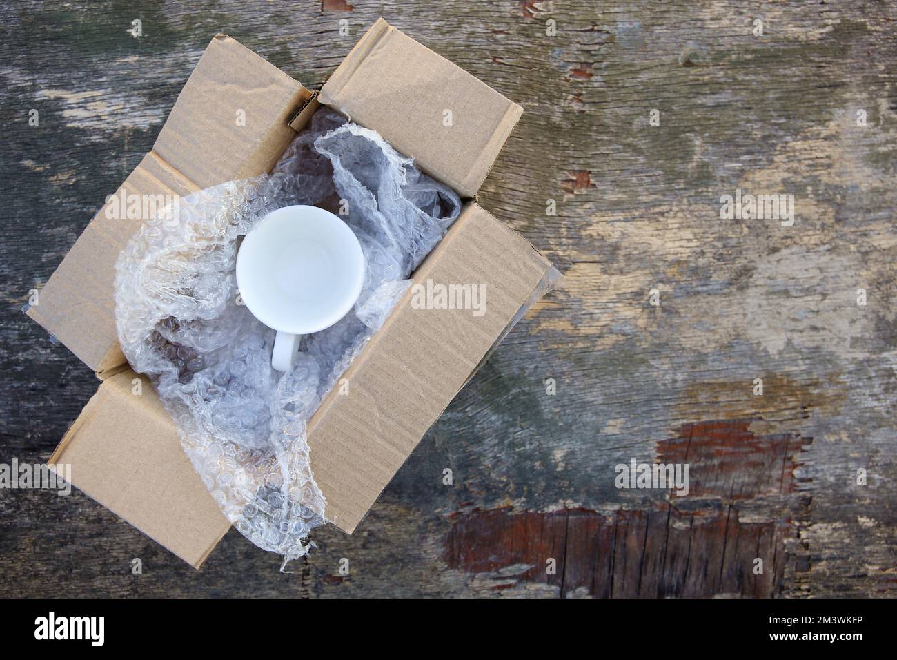 Packed cup in a plastic bubble wrap on an old wooden background. Fragile package. Stock Photo