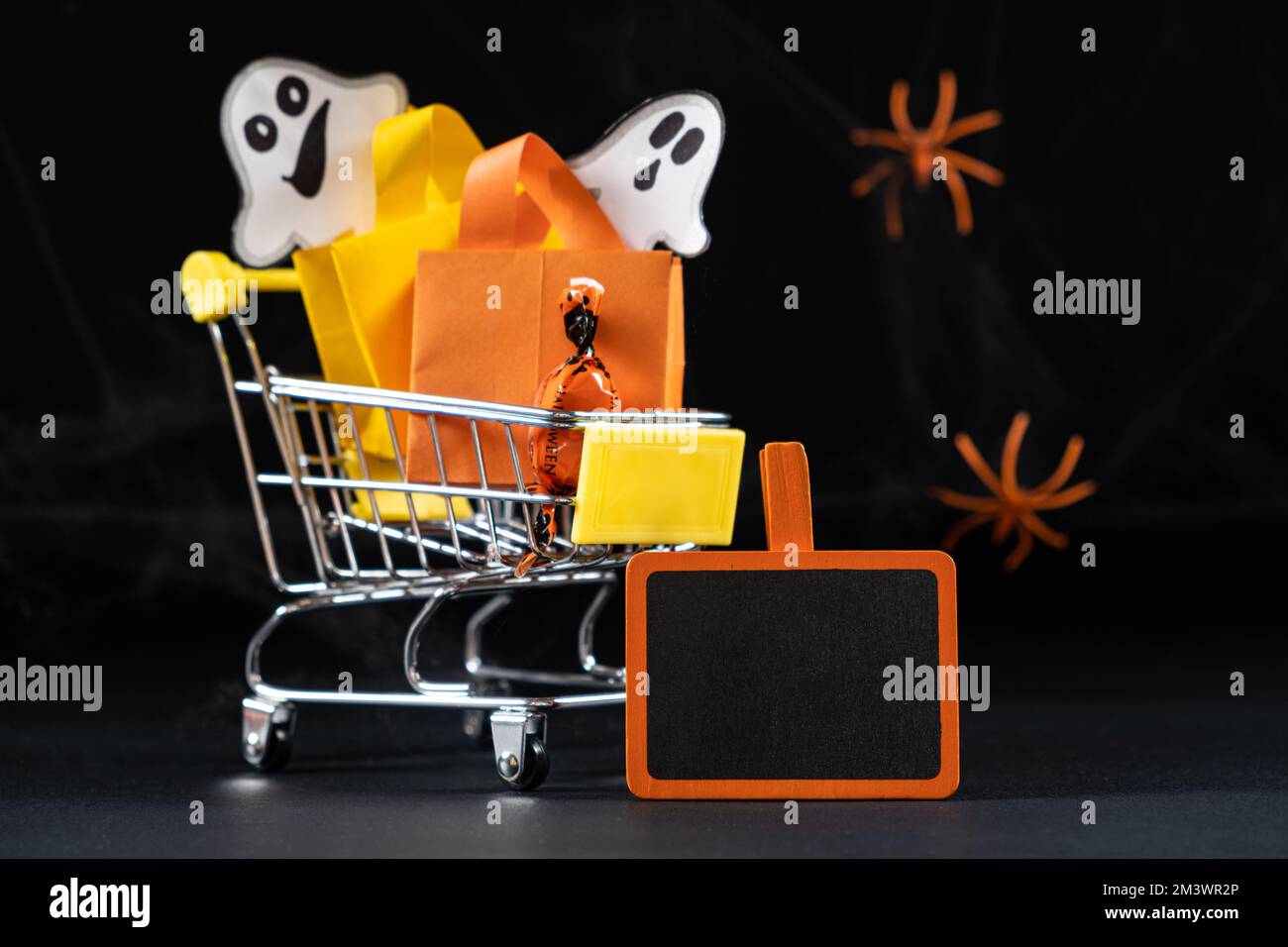 A small cart with bags, gifts and ghosts on the black background. Halloween Sale, space for text. Stock Photo