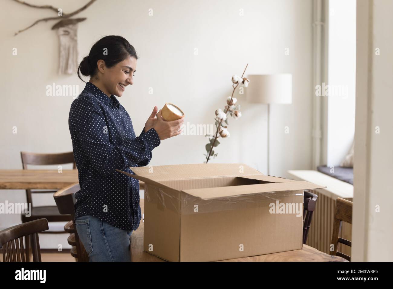 Happy young Indian renter girl packing stuff for leaving apartment