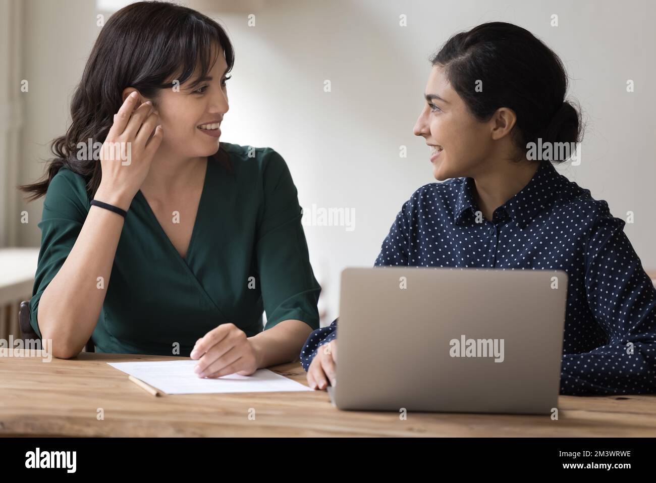 Happy multiethnic female office friends talking at workplace Stock Photo