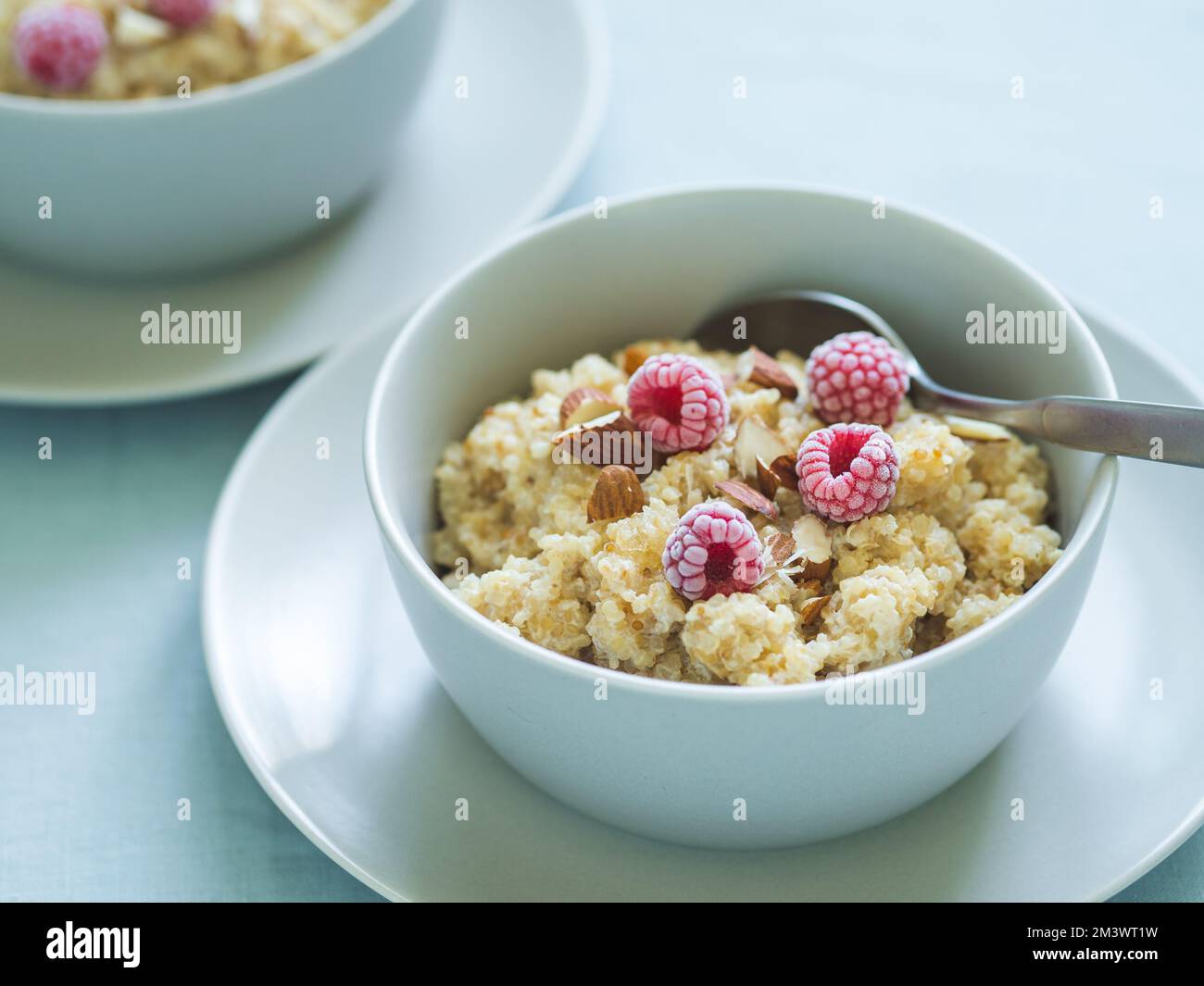 Quinoa porrige on tabletop. Two bowl wit quinoa milk porridge with berries and almond. Frozen raspberries in quinoa porrige Stock Photo